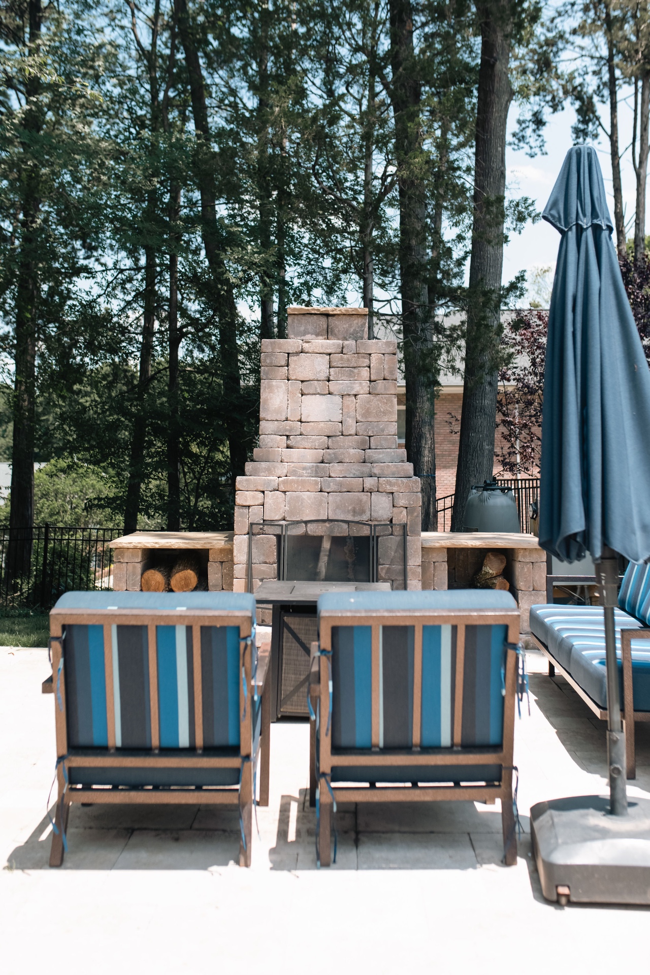 Stone outdoor fireplace with built-in wood storage benches and poolside lounge seating.