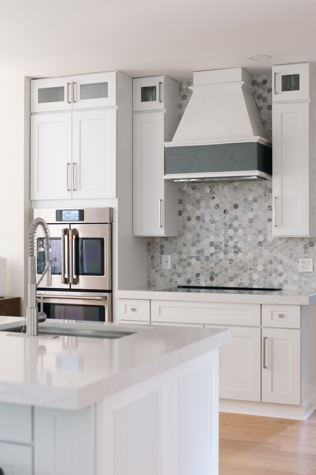 Range wall detail with custom hood, marble hex tile backsplash, and stainless double ovens.