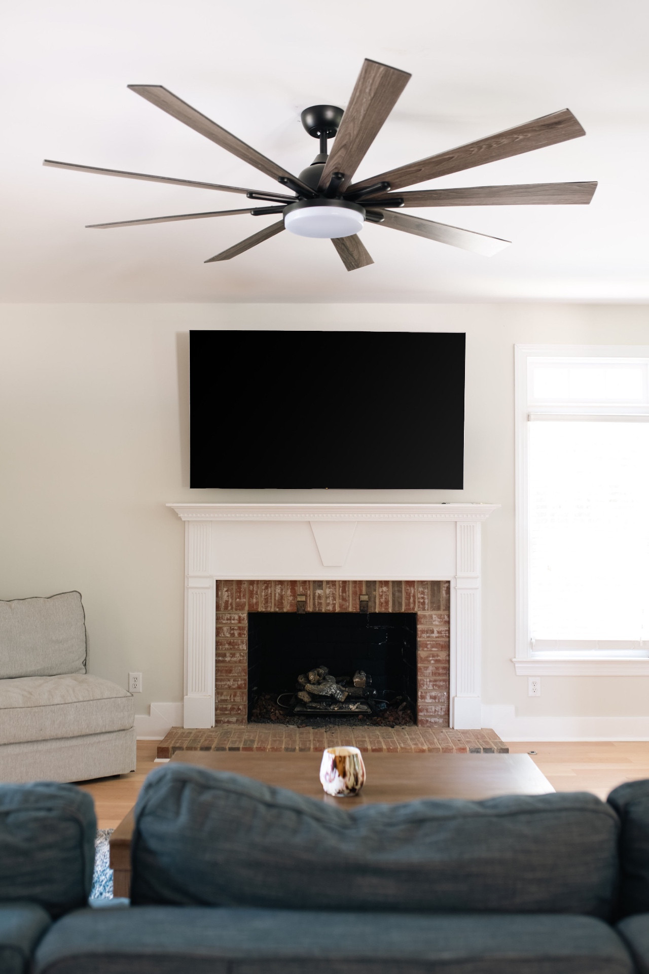 Family room with brick wood-burning fireplace, mounted TV, and oversized windmill ceiling fan.
