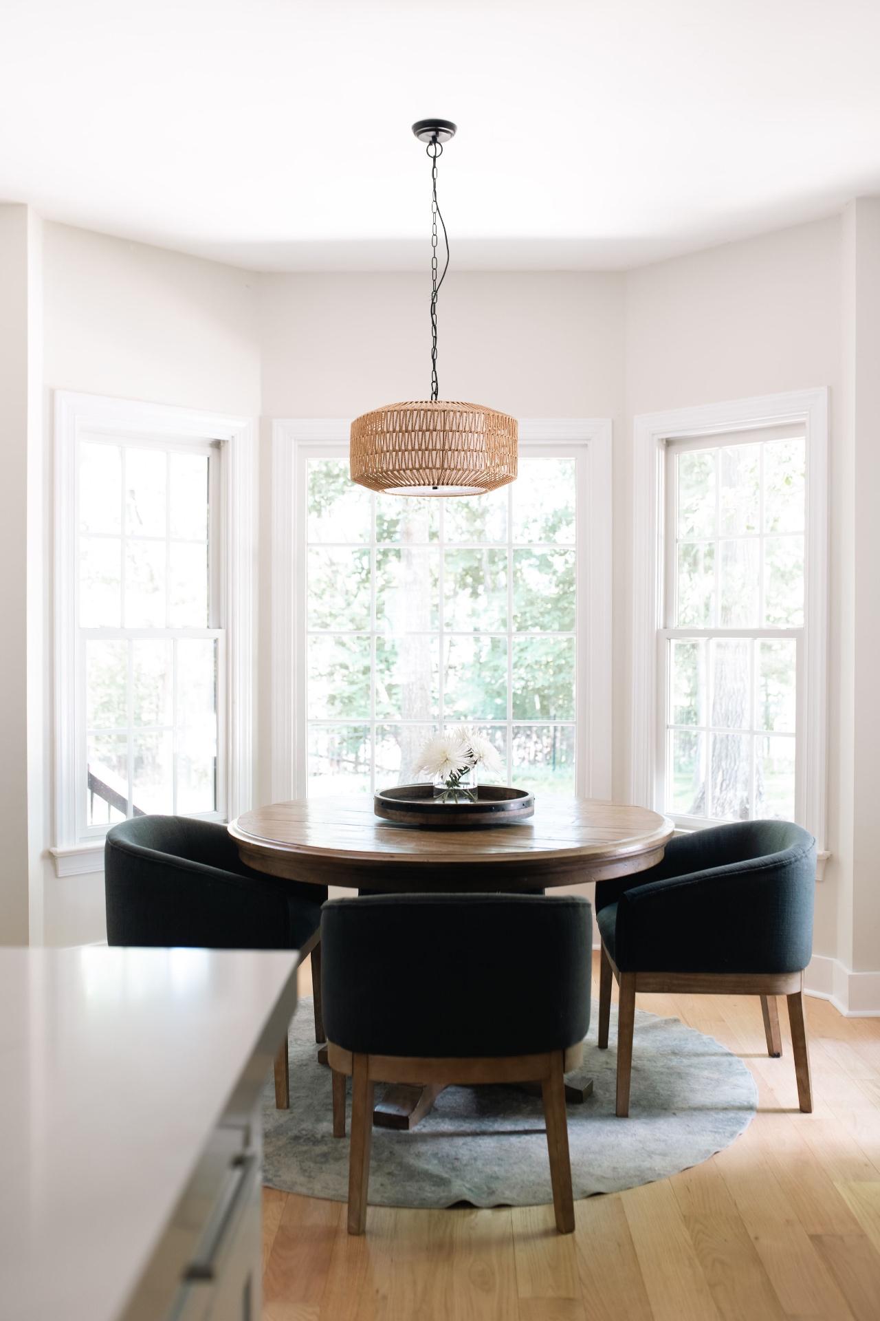 Sun-filled breakfast nook with bay windows, round pedestal table, and woven pendant.
