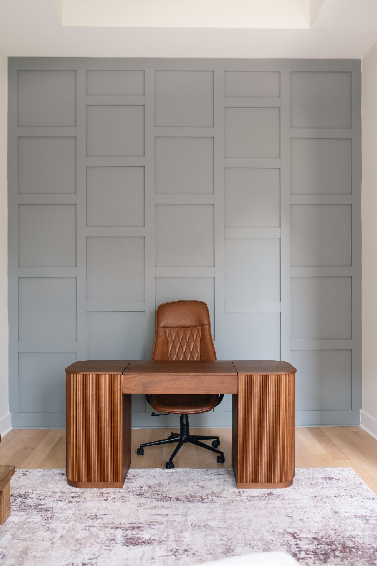 Main-level office with custom sage board-and-batten accent wall and fluted wood desk.