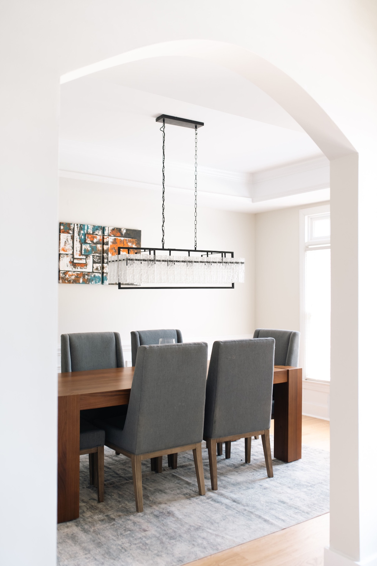 Formal dining room with linear glass chandelier, walnut table, and tray ceiling.