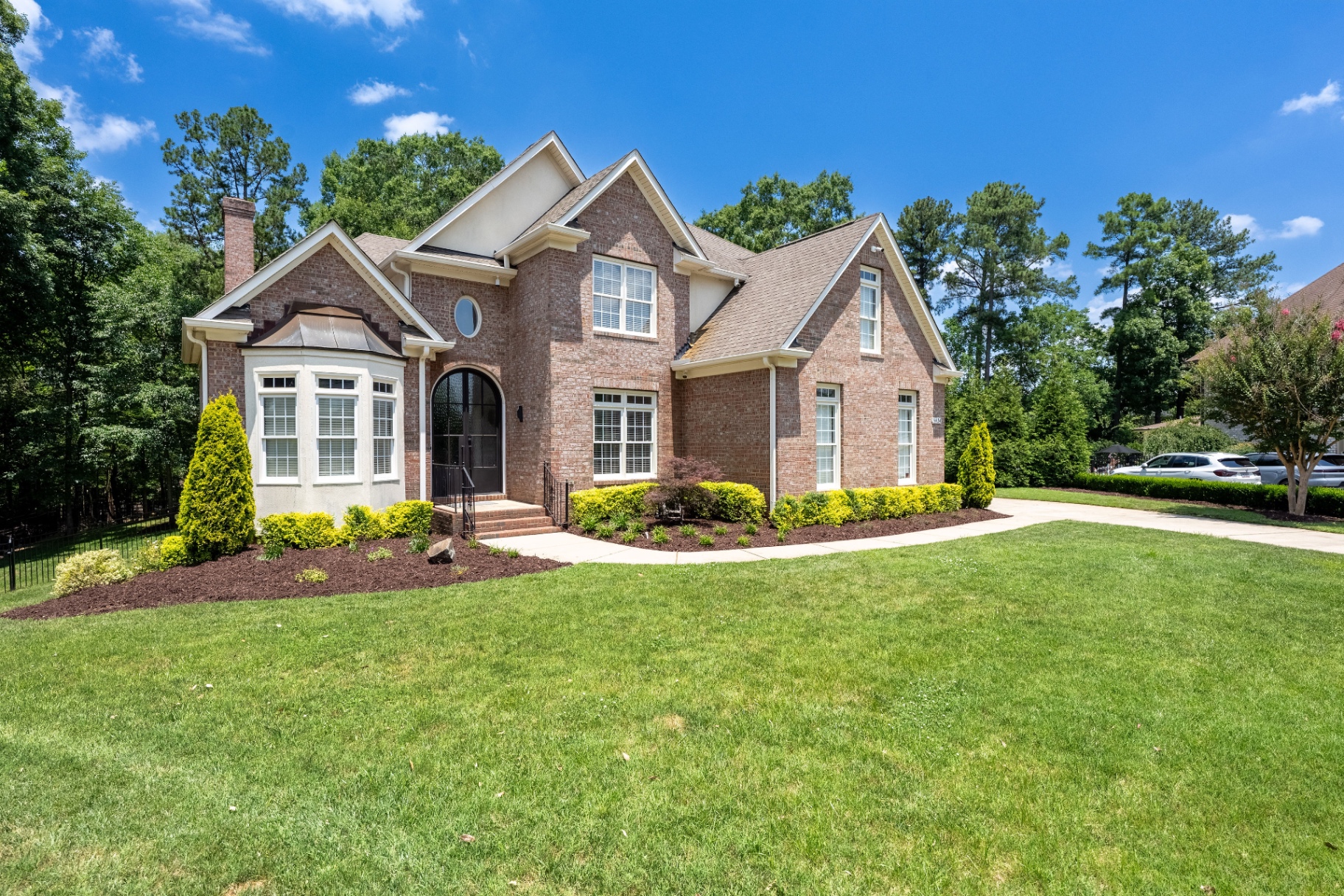 Front elevation highlighting the arched entry, mature landscaping, and broad front lawn.