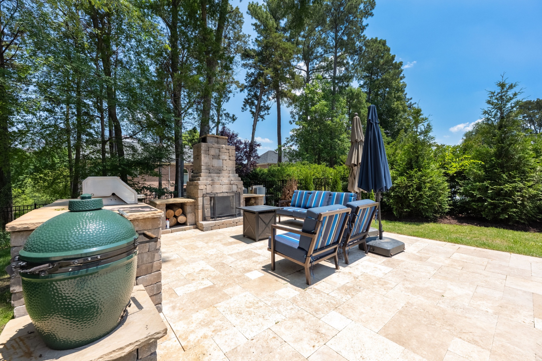 Outdoor kitchen and fireplace gathering area framed by mature privacy landscaping.
