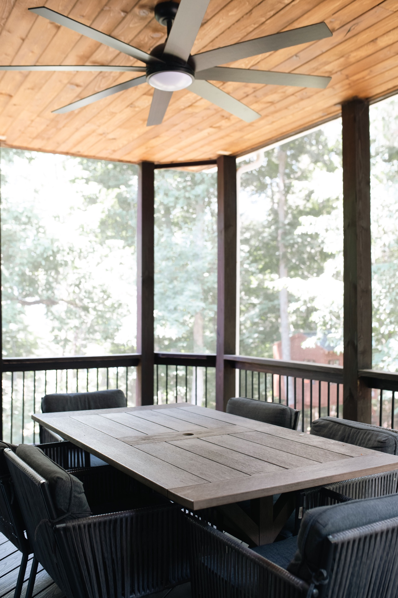 Screened porch with tongue-and-groove wood ceiling, large fan, and outdoor dining set overlooking the woods.