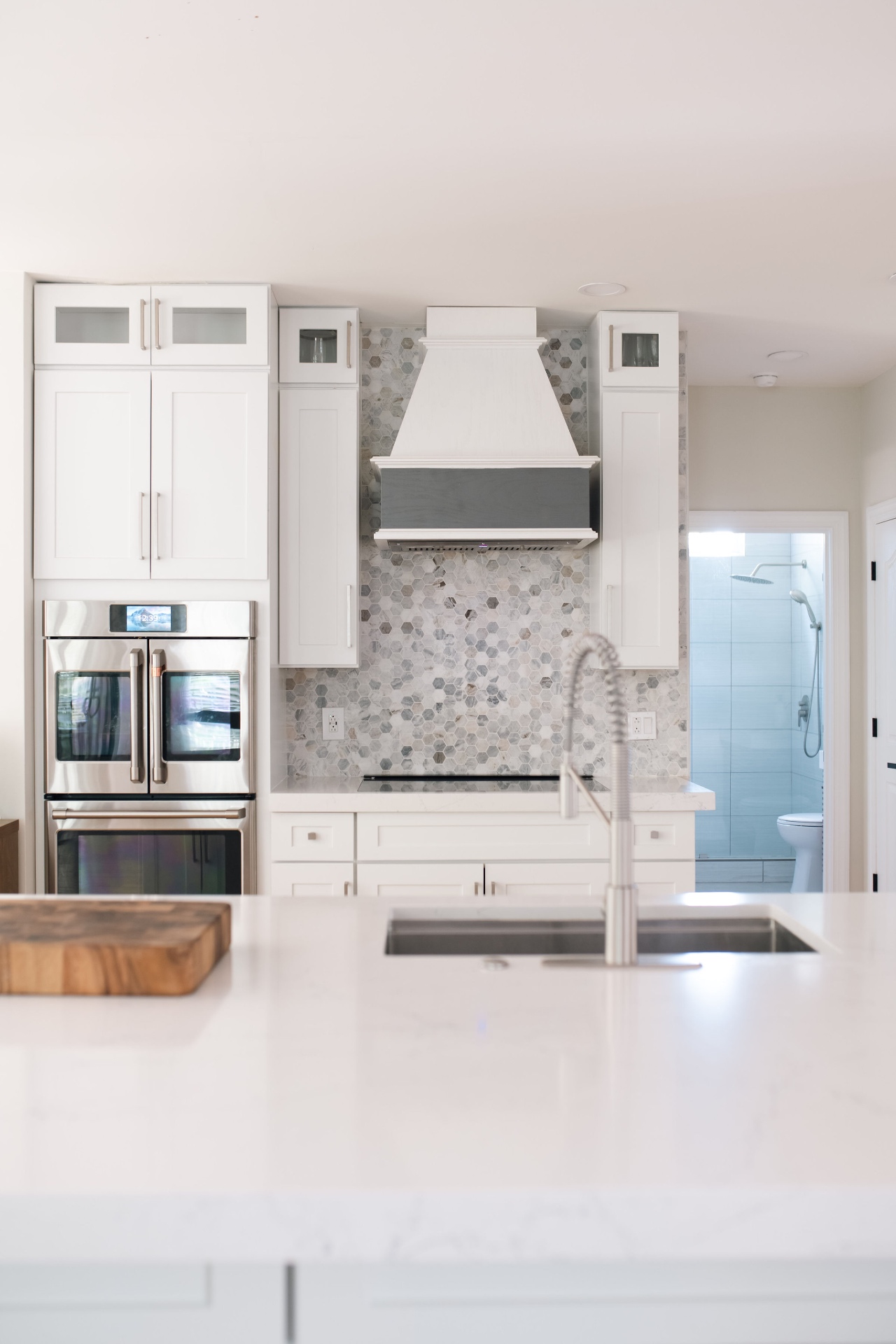 Quartz island with prep sink looking toward the range, vent hood, and double ovens.