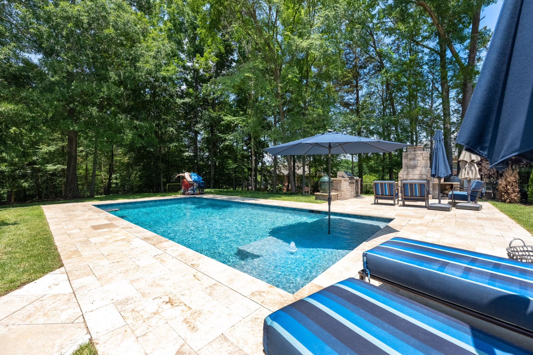 Sparkling saltwater pool with expansive tanning ledge and private wooded backdrop.