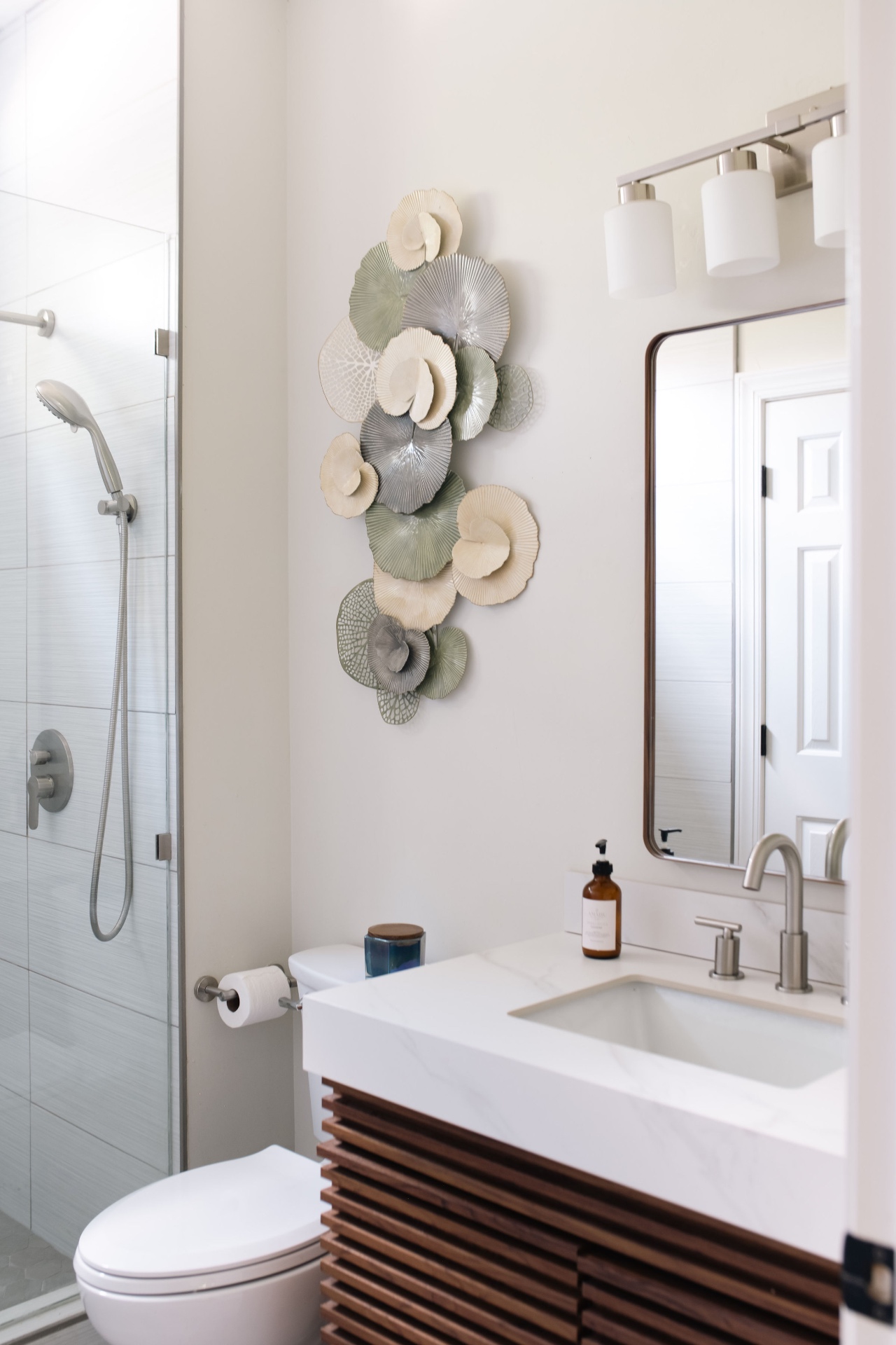 Guest bath with walk-in shower, floating slatted wood vanity, and sculptural wall art.