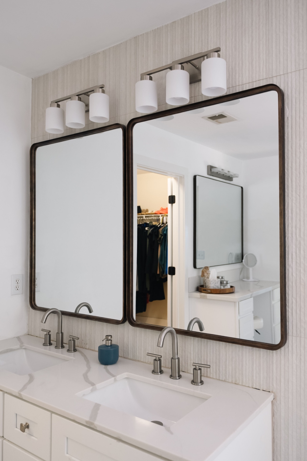 Primary bath double vanity with quartz counters, arched wood-framed mirrors, and walk-in closet beyond.