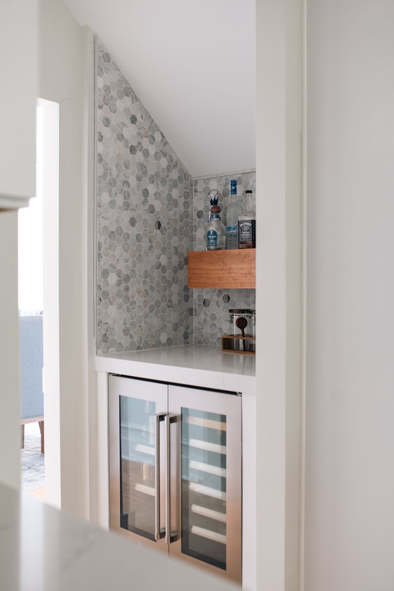 Built-in wet bar nook with marble hex tile, floating shelf, and dual beverage refrigerators.