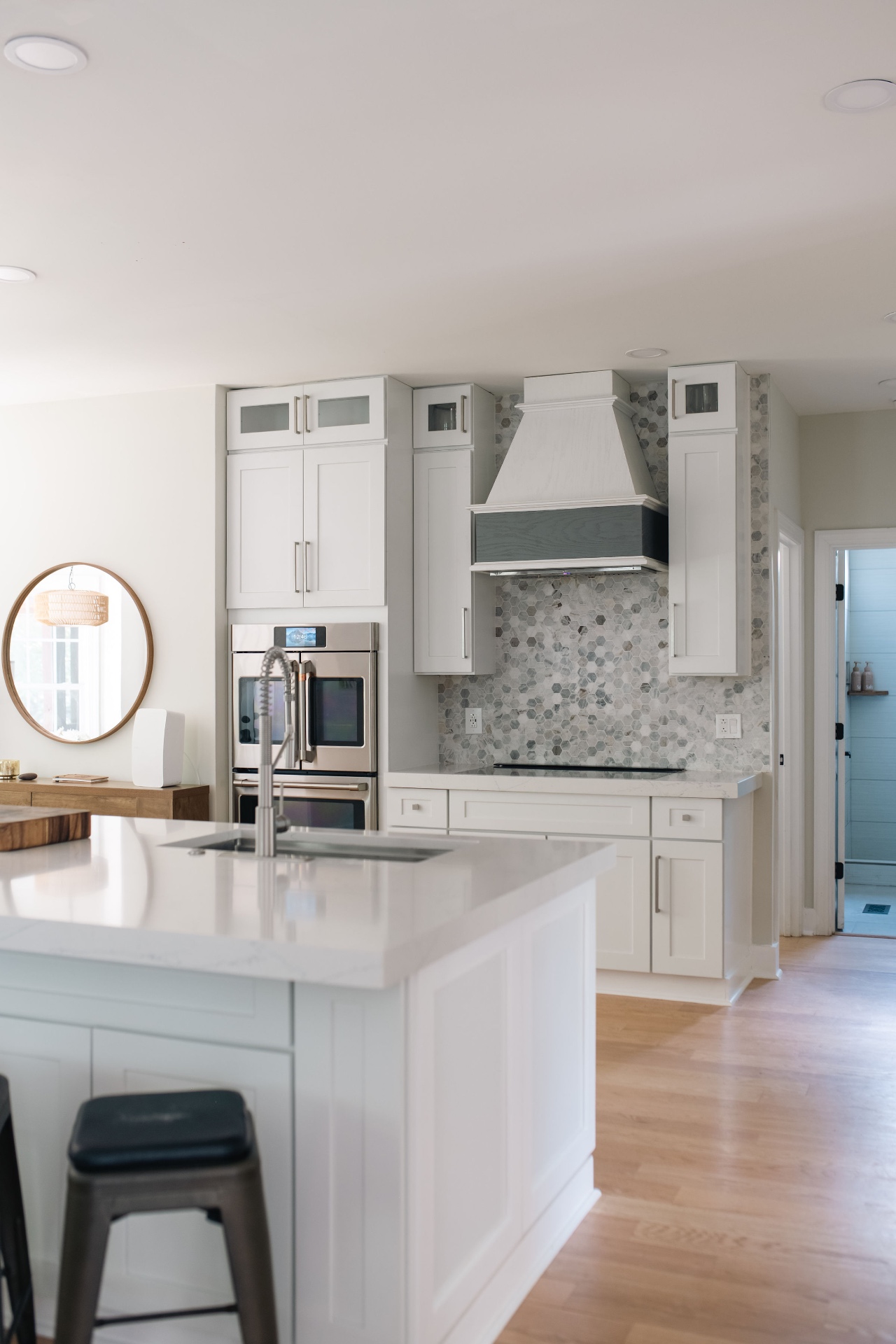 Chef's kitchen with custom vent hood, double wall ovens, induction cooktop, and marble hex backsplash.