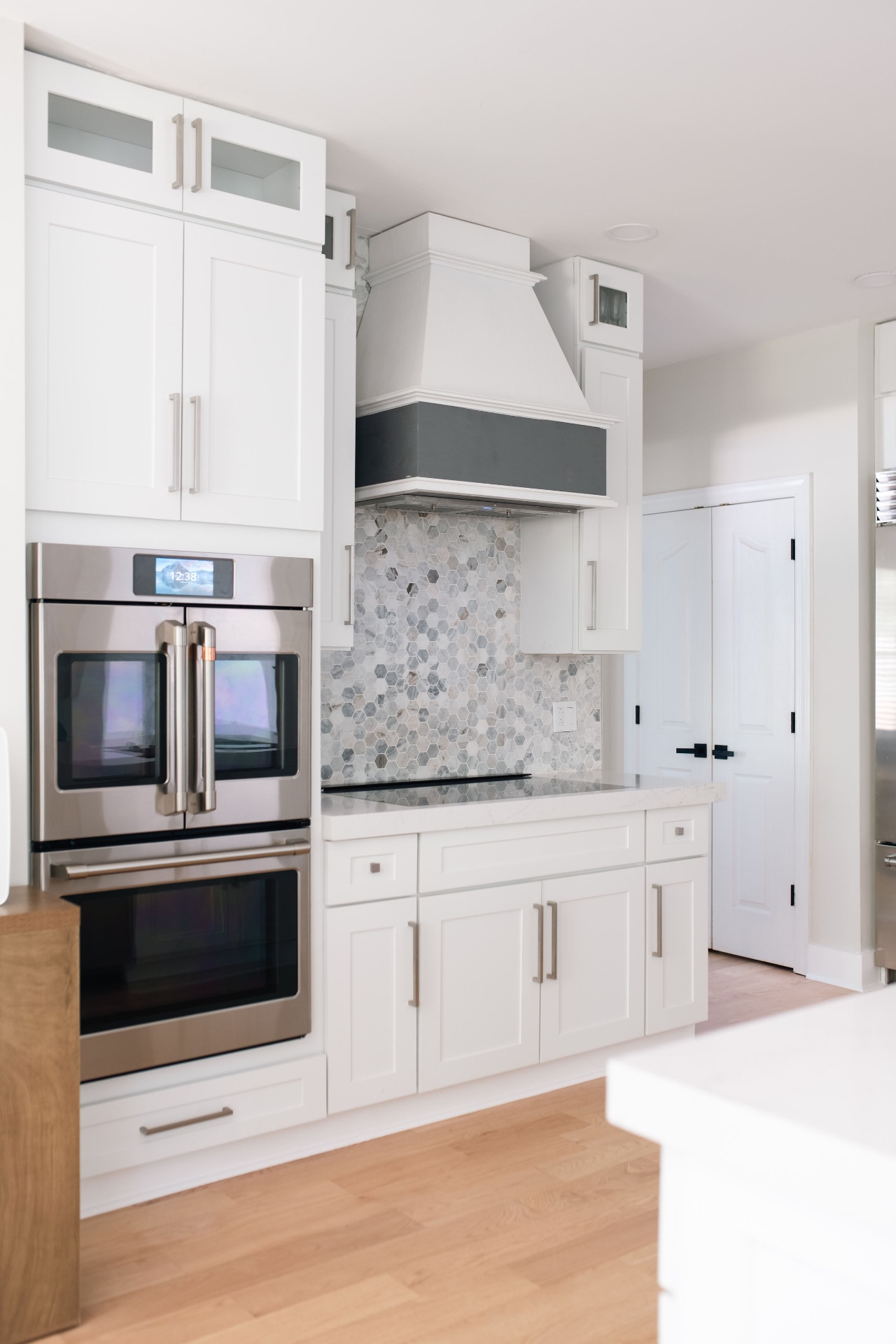 Café double oven, induction cooktop, custom vent hood, and marble hex backsplash.