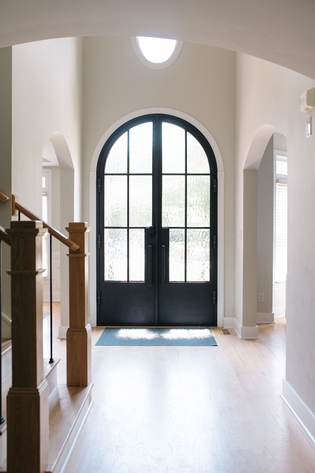 Two-story foyer with custom arched steel double front doors and oculus window above.