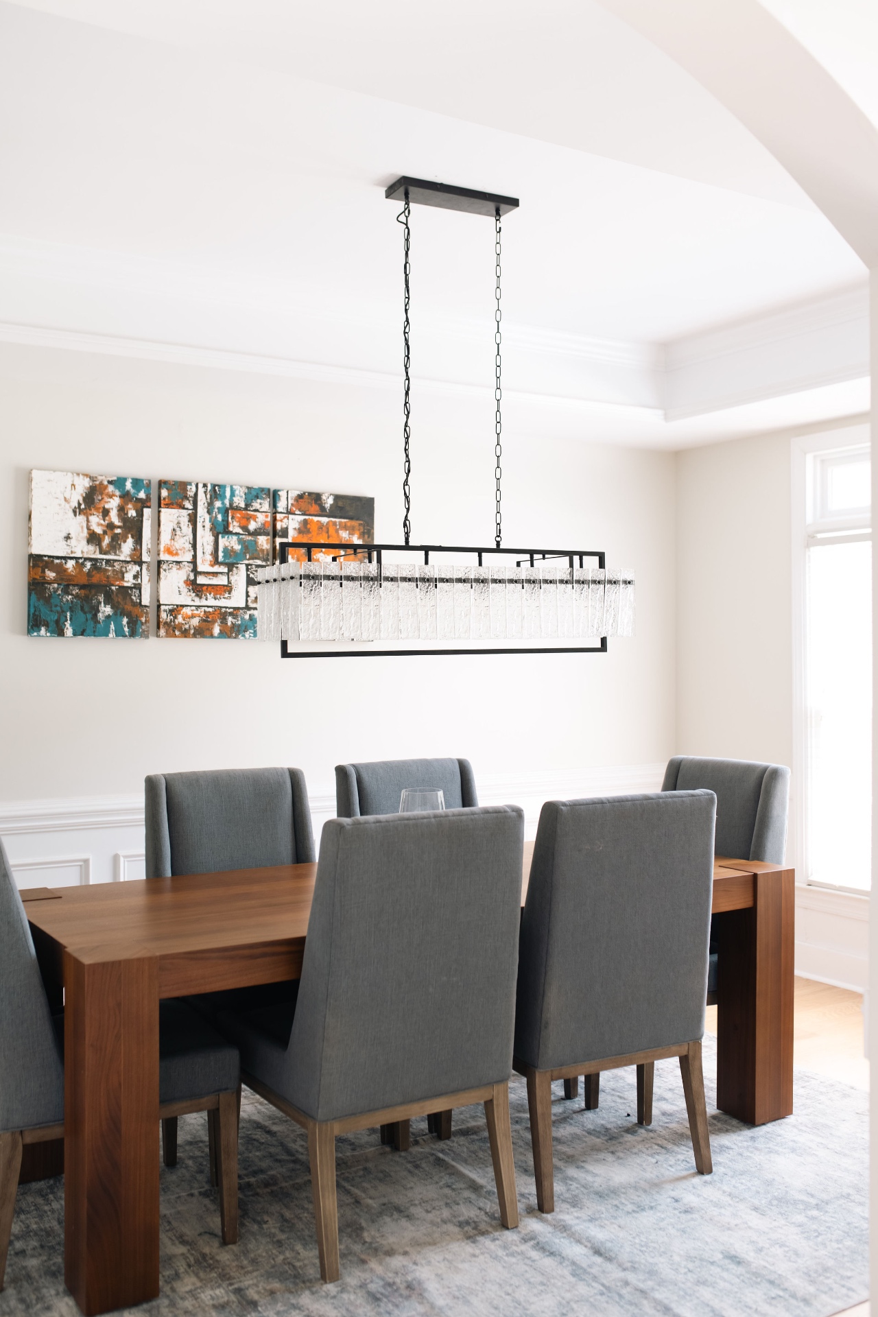 Formal dining room with walnut table, upholstered chairs, and linear crystal chandelier.